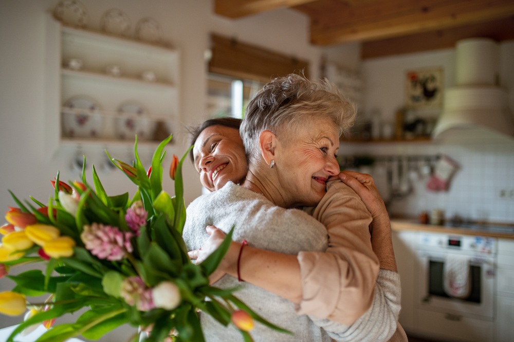 Una mamma anziana felice che abbraccia la figlia adulta in casa, in occasione della festa della mamma o di un compleanno.