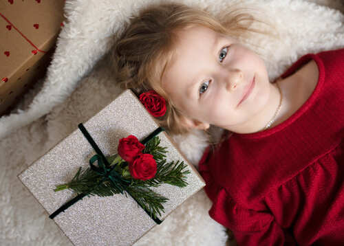 Bambina sdraiata accanto a una confezione regalo decorata con rose rosse e rametti verdi