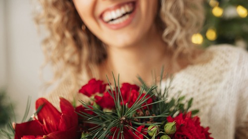 Primo piano di bouquet natalizio con fiori rossi e rametti verdi tenuto da una donna sorridente
