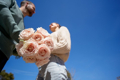 Coppia all’aperto che si guarda sorridendo mentre tiene un bouquet di rose rosa