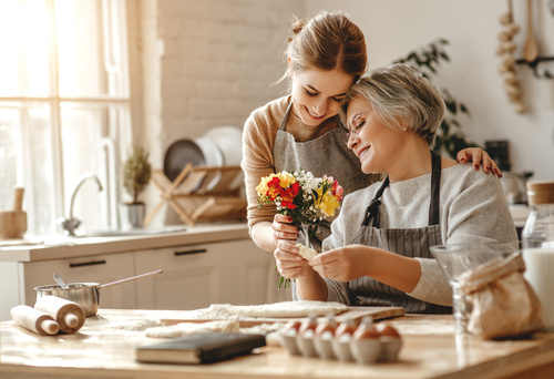 happy mother's day! family old grandmother mother-in-law and daughter-in-law daughter congratulate on holiday, give flowers Figlia adulta regala un piccolo bouquet alla madre mentre trascorrono un momento insieme in cucina preparando dolci.